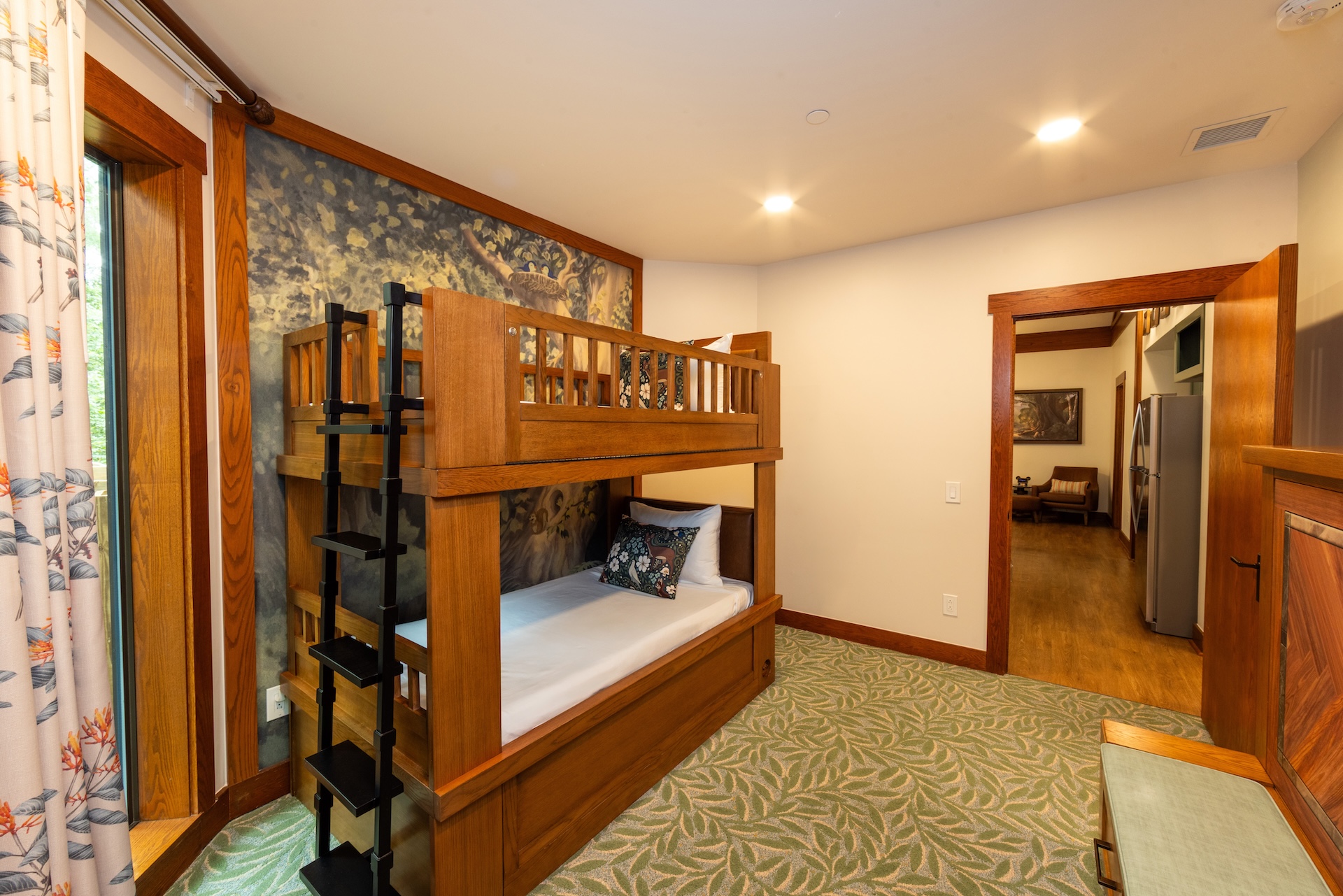 Saratoga Springs new DVC villas. The image features a well-furnished room with a wooden bunk bed and a patterned carpet. Natural light filters in through large windows, highlighting the cozy atmosphere of the space.