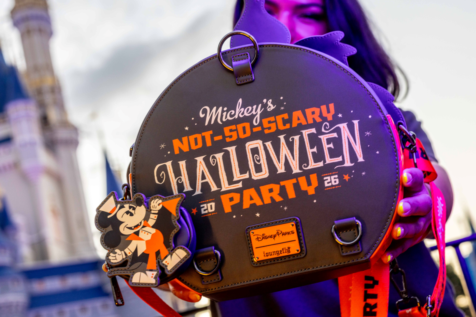 A person holds a themed backpack featuring Disney's Mickey Mouse at a Halloween event. The backpack displays text indicating 'Mickey's Not-So-Scary Halloween Party 2026', with a prominent illustration of Mickey.