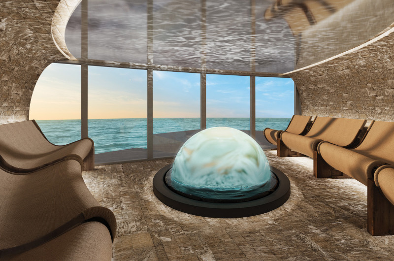 The image depicts a modern, serene interior space featuring a circular, water-themed installation at its center. Large windows provide a breathtaking view of the ocean and sky at sunset.