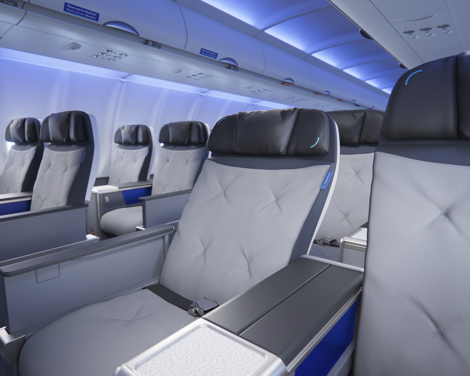 The image features a row of aircraft seating inside a modern airplane cabin. The seats are upholstered in gray fabric with black headrests and show a sleek, contemporary design under soft blue ambient lighting.