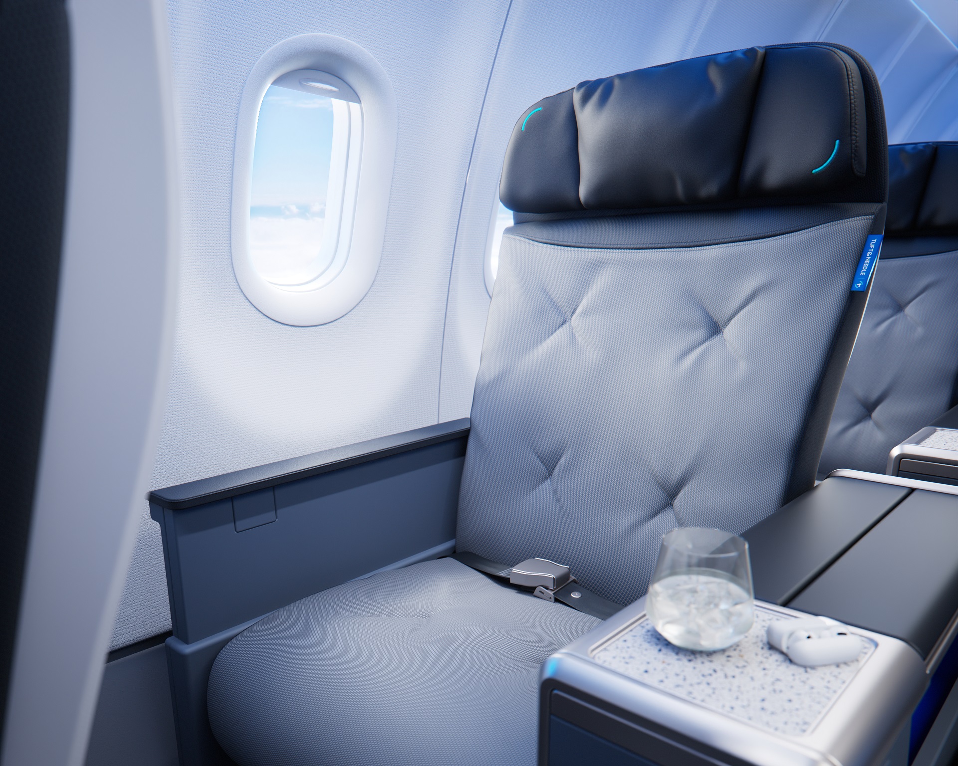 The image depicts the interior of an airplane cabin, showcasing a comfortable seating area. The plush, grey seat is beside a window, with a compact table displaying a glass of water and a pair of headphones.