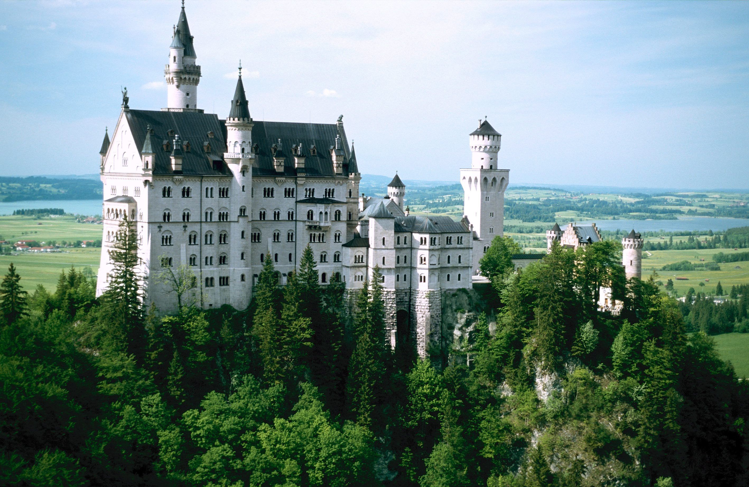 The image showcases Neuschwanstein Castle, a picturesque 19th-century Romanesque Revival palace nestled in the Bavarian Alps of Germany. Surrounded by lush greenery and overlooking a serene lake, the castle is renowned for its fairy tale-like appearance and intricate architectural details.
